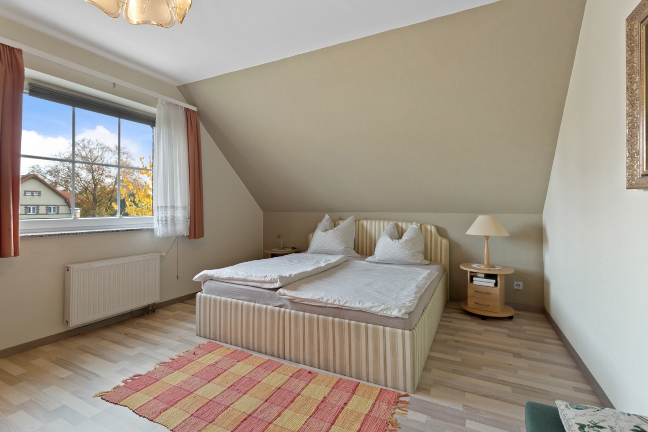 Helles Schlafzimmer mit Doppelbett, Nachttisch, Stehlampe und großem Fenster.