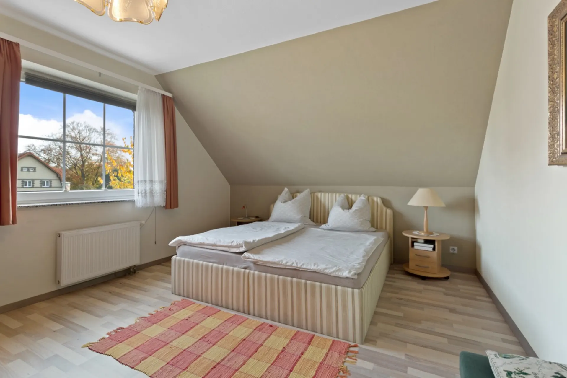 Helles Schlafzimmer mit Doppelbett, Nachttisch, Stehlampe und großem Fenster.