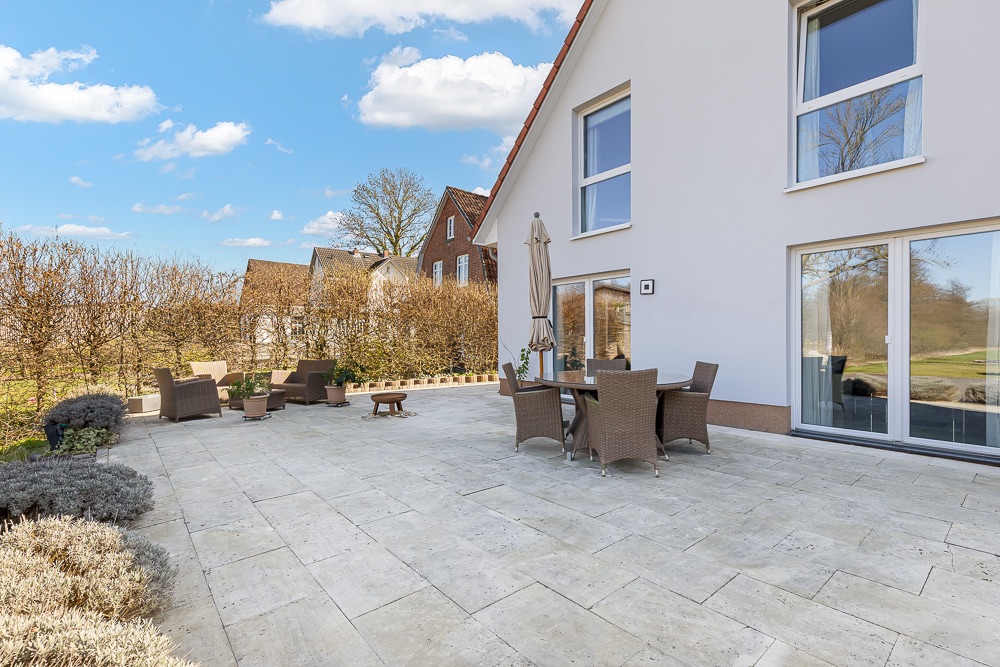 Große Terrasse mit Esstisch, Stühlen und Sesseln an einem modernen Wohnhaus.