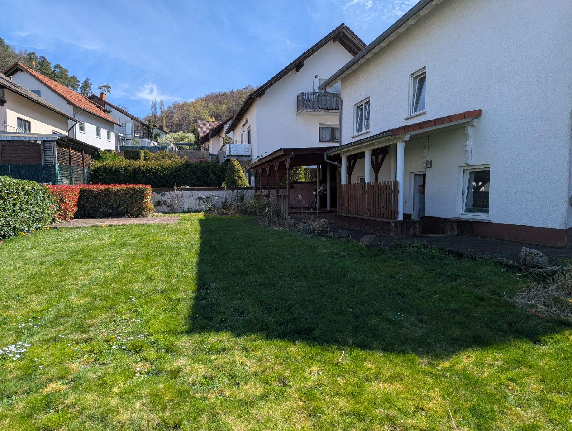 Großer Garten mit Rasenfläche vor einem weißen Wohnhaus, umgeben von weiteren Häusern.