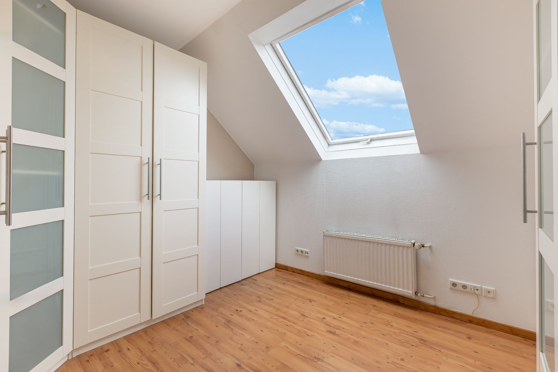 Heller Raum mit Holzfußboden, weißen Schränken und großem Dachfenster.