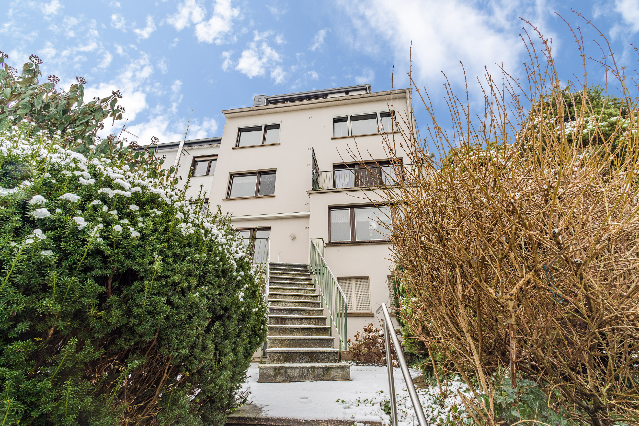 Mehrstöckiges Wohnhaus mit Treppe und winterlicher Bepflanzung im Vordergrund.