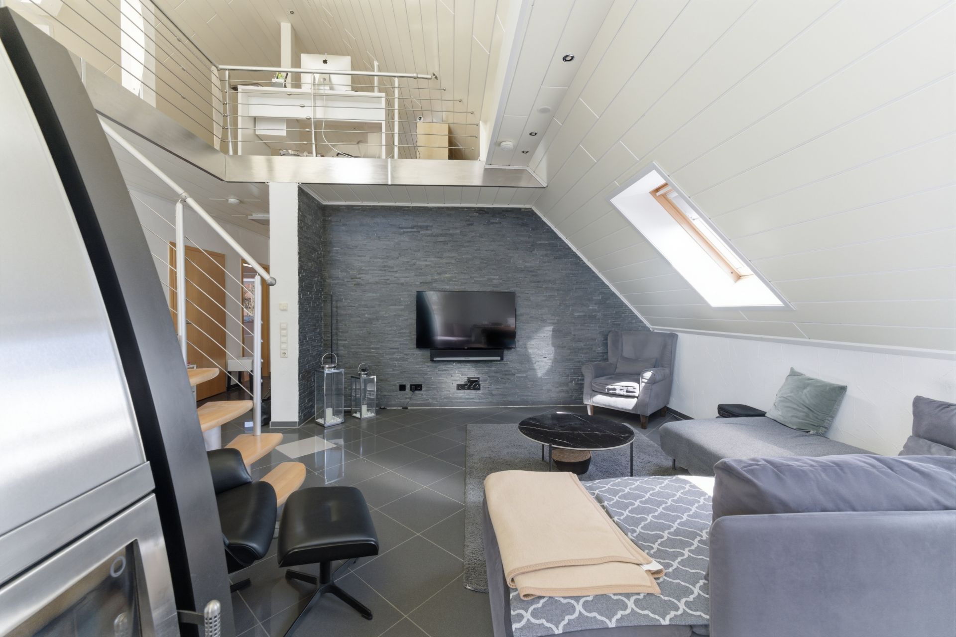 Modernes Wohnzimmer mit Ecksofa, Fernseher, Sessel und Galerie mit Arbeitsplatz im Obergeschoss.