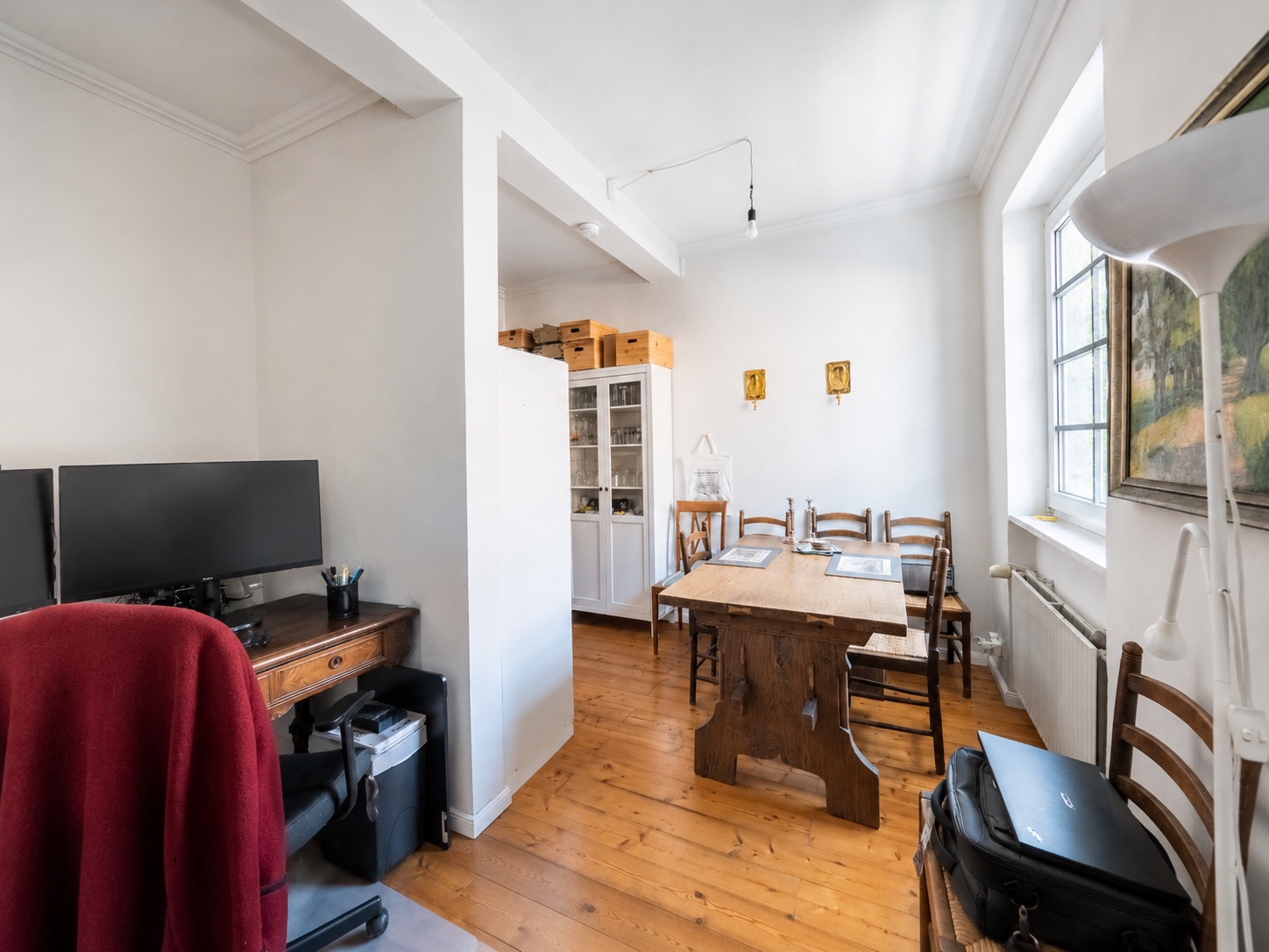 Wohnzimmer mit Holztisch, Stühlen, Schreibtisch mit Monitoren und Fenster.