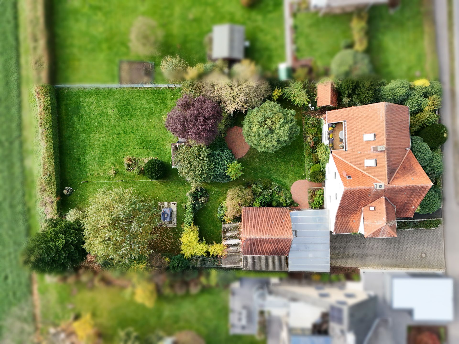 Luftaufnahme eines Hauses mit rotem Dach und großem Garten mit Bäumen und Rasen.
