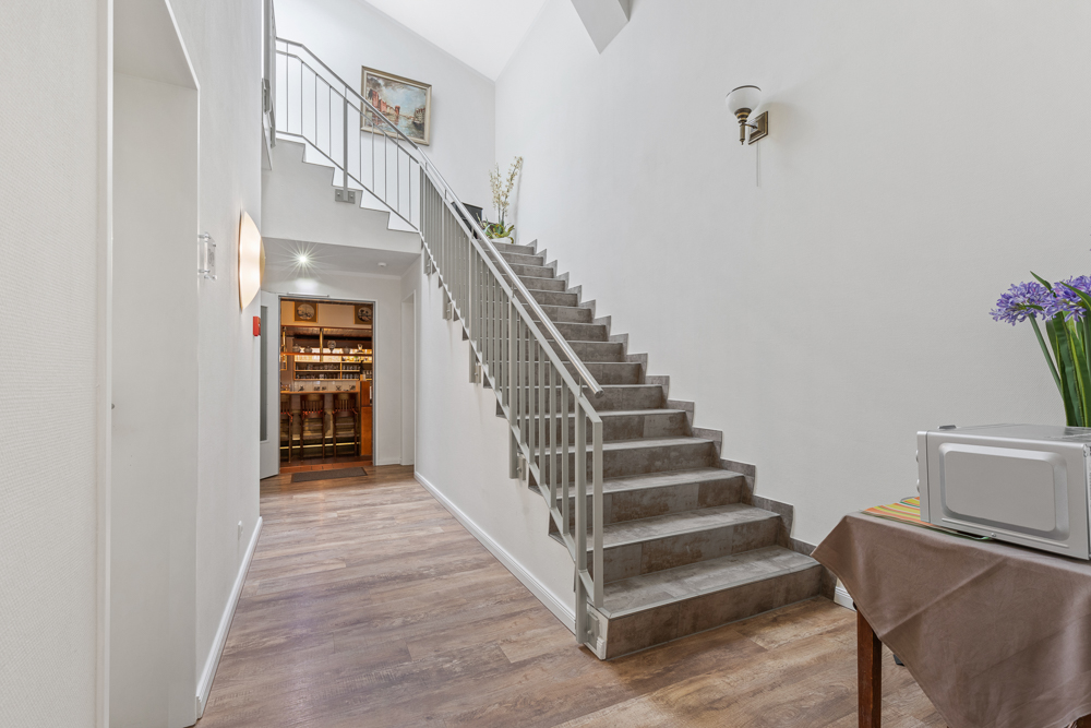 Flur mit Holzfußboden, Treppe nach oben, Tisch mit Mikrowelle und Blumen, Regal im Hintergrund.