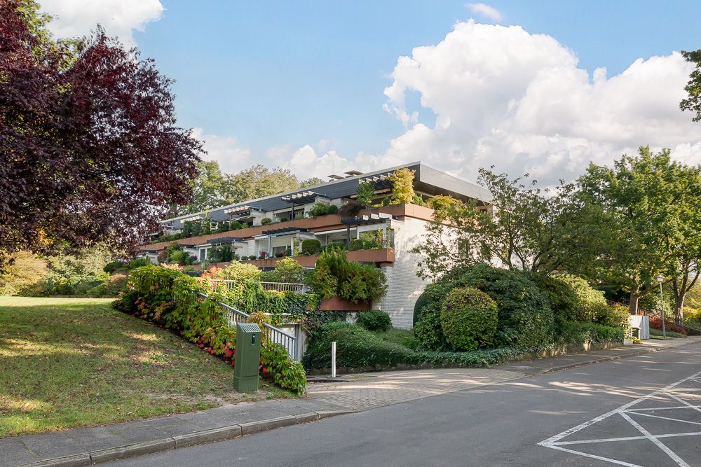 Modernes Wohngebäude mit mehreren Balkonen und viel Grün an einer ruhigen Straße.