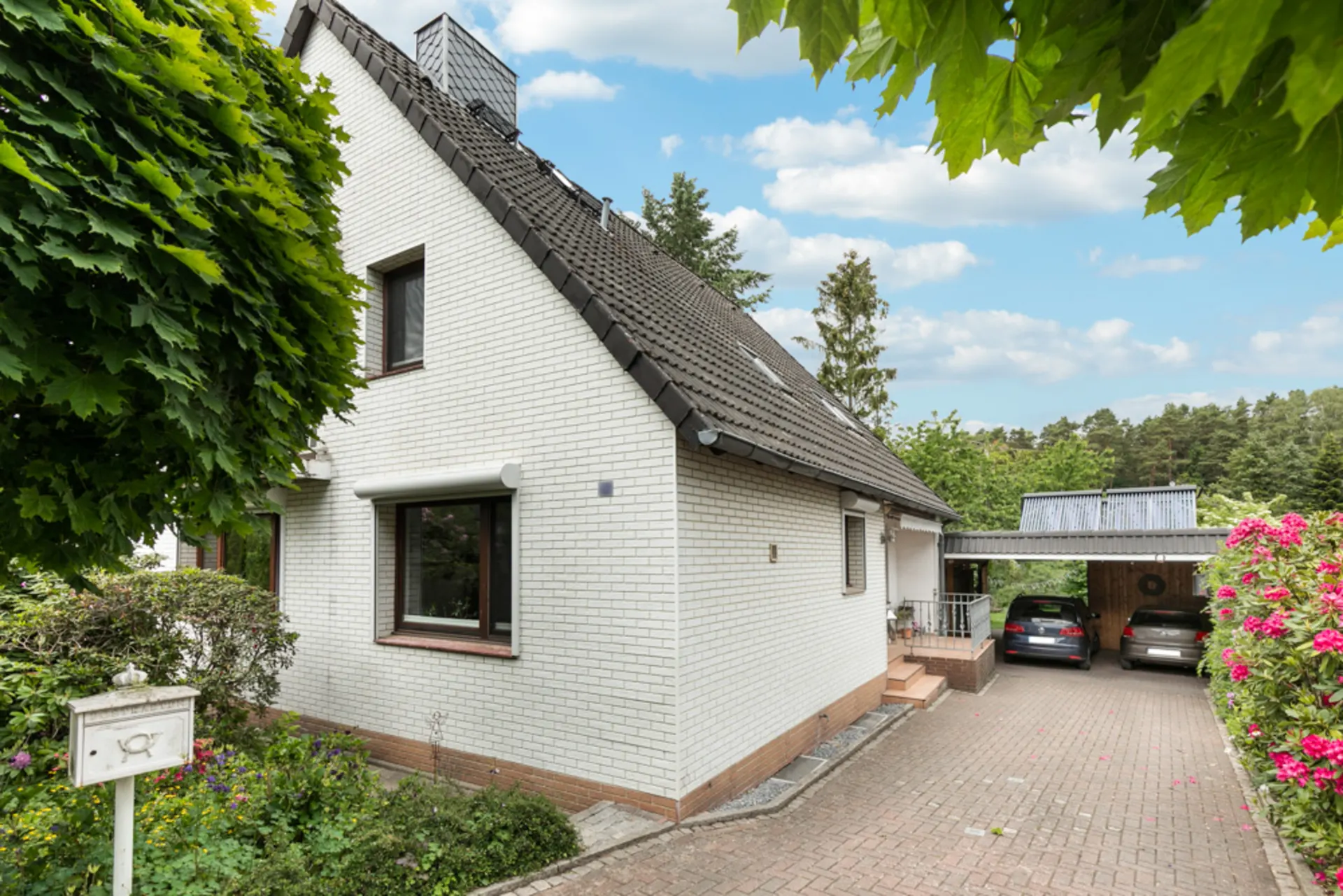 Weißes Einfamilienhaus mit Satteldach, Vorgarten und Carport mit zwei Autos.