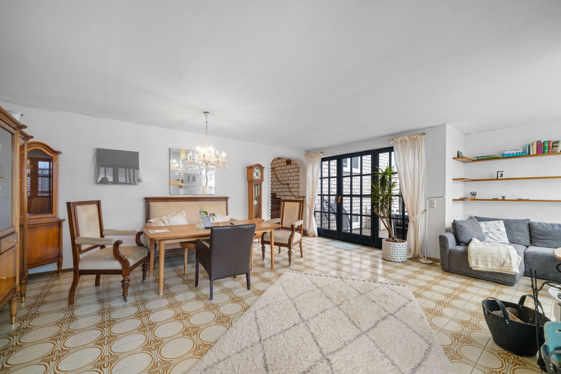 Helles Wohnzimmer mit Esstisch, Stühlen, Sofa, Regal, Teppich und großen Fenstern.