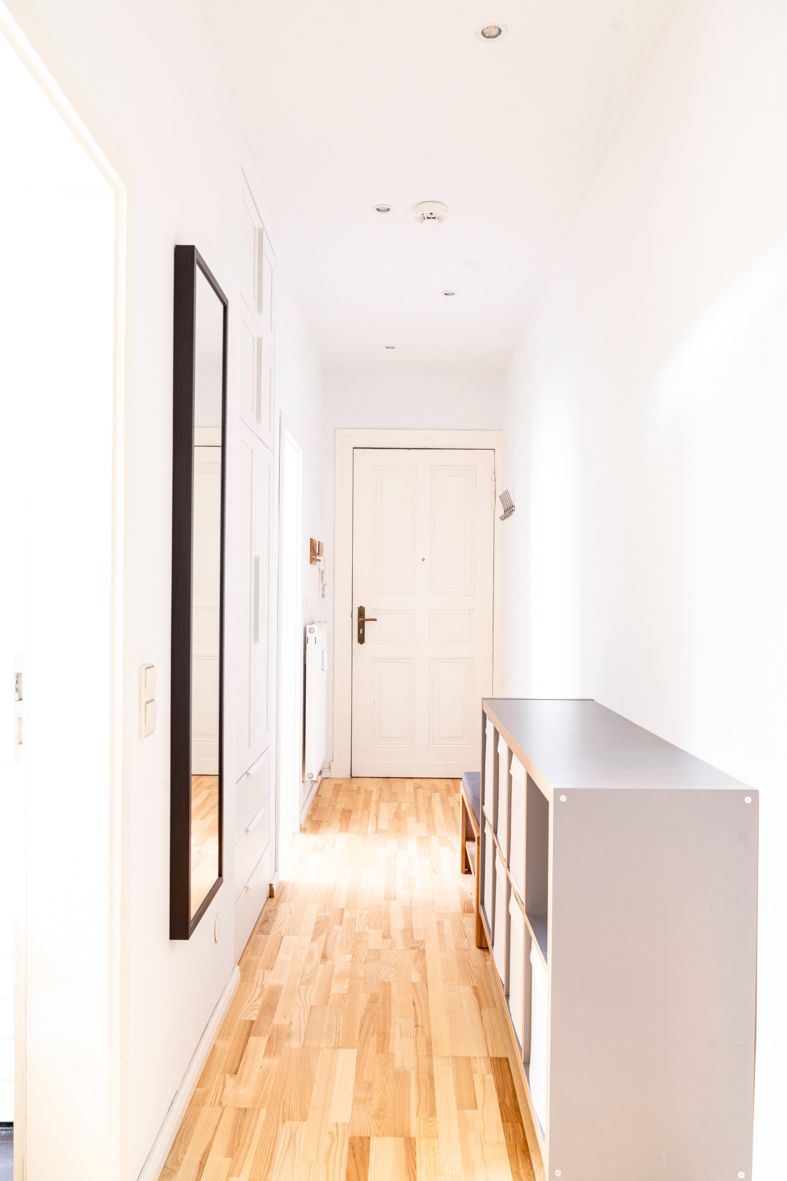 Heller Flur mit Holzfußboden, Regal, Spiegel und weißer Eingangstür.