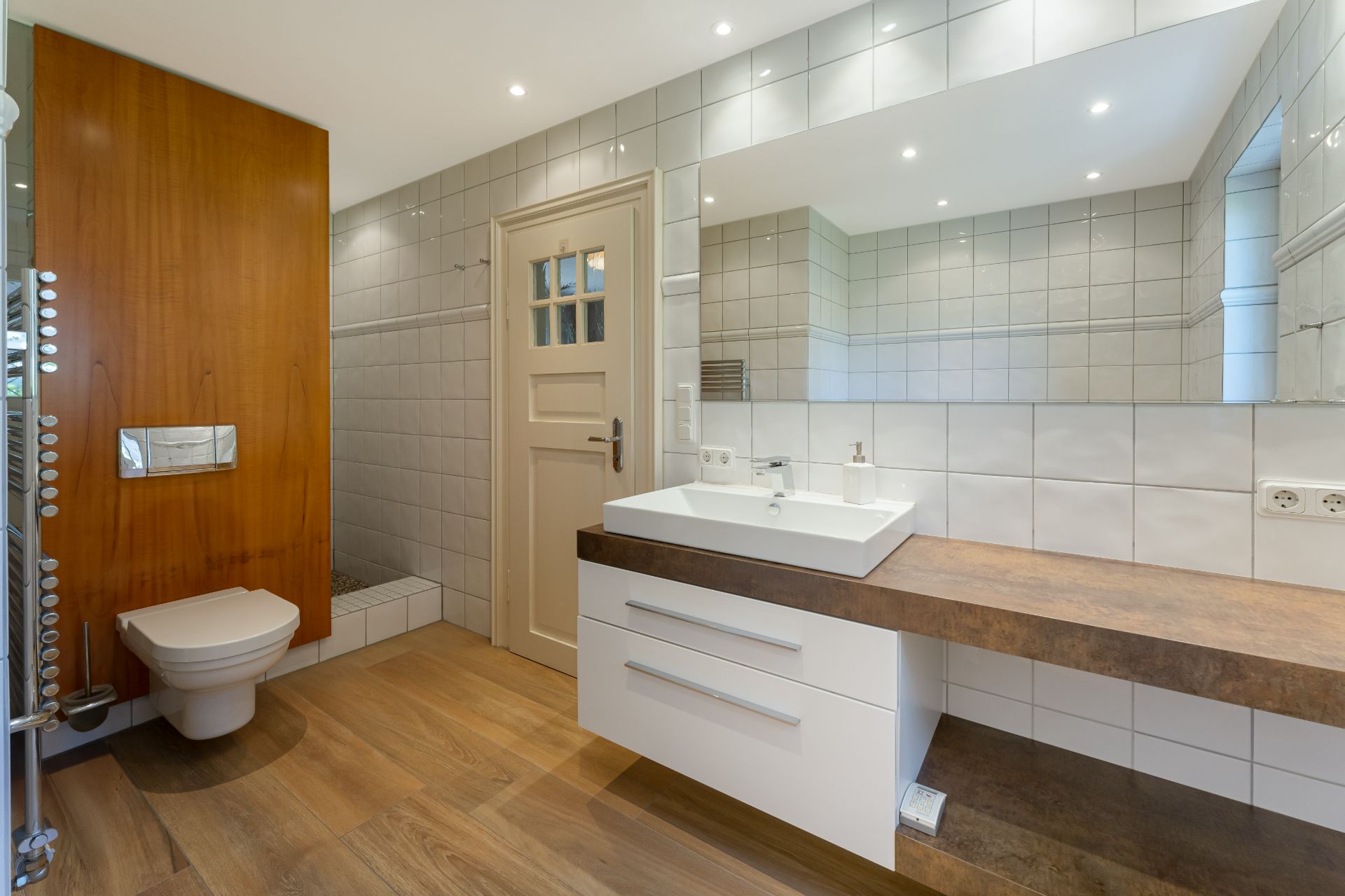 Modernes Badezimmer mit Holzfußboden, weißer Wand, Waschbecken und wandhängendem WC.