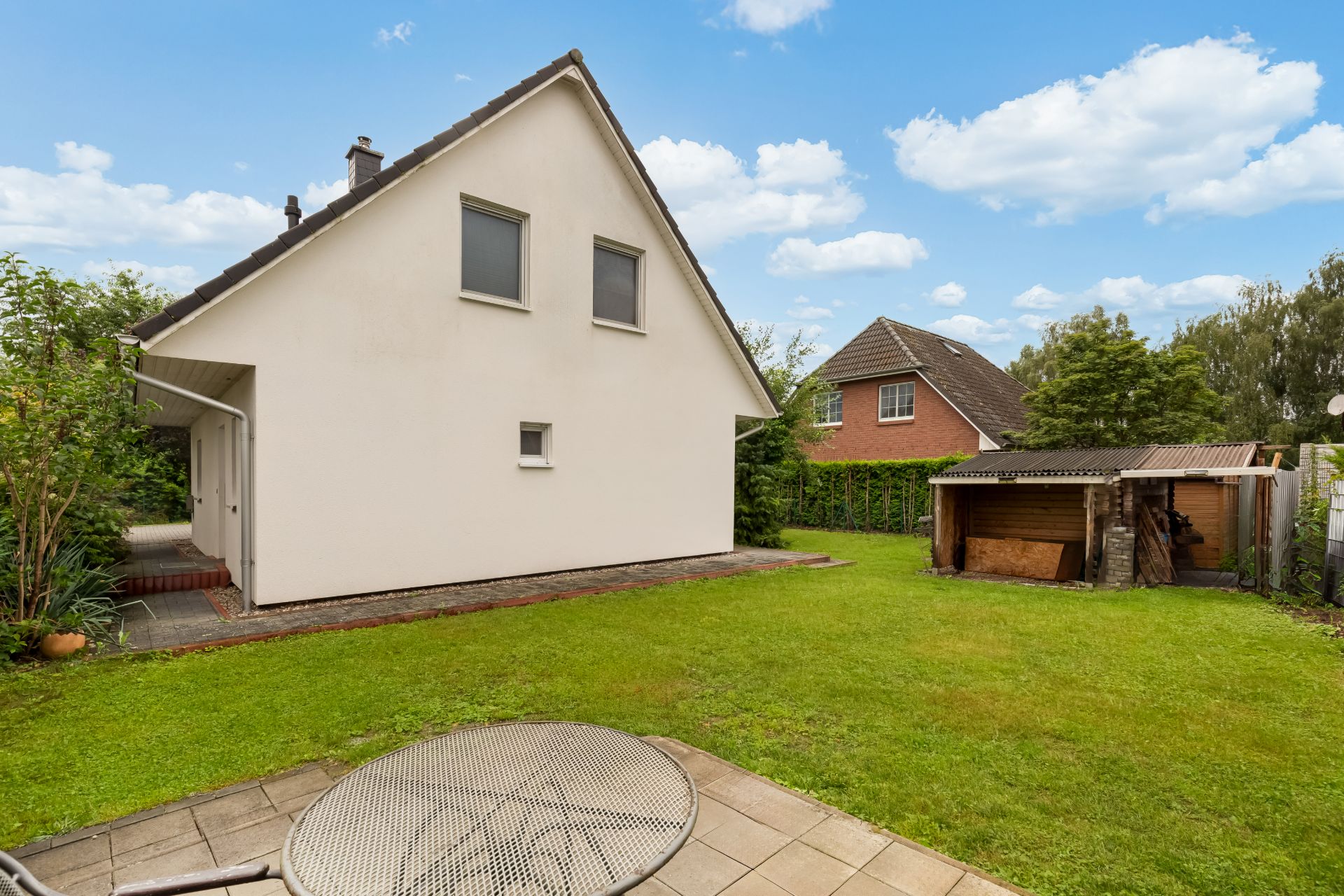 Garten mit Rasenfläche, Terrasse, Nebengebäude und Blick auf ein Einfamilienhaus.