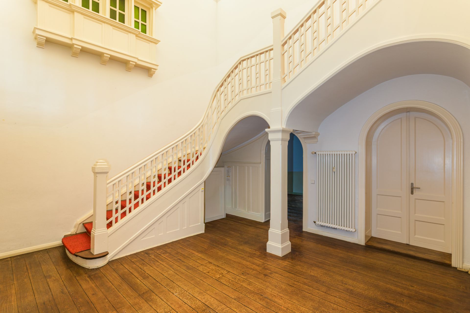 Heller Flur mit geschwungener Treppe, Holzfußboden und weißen Türen.