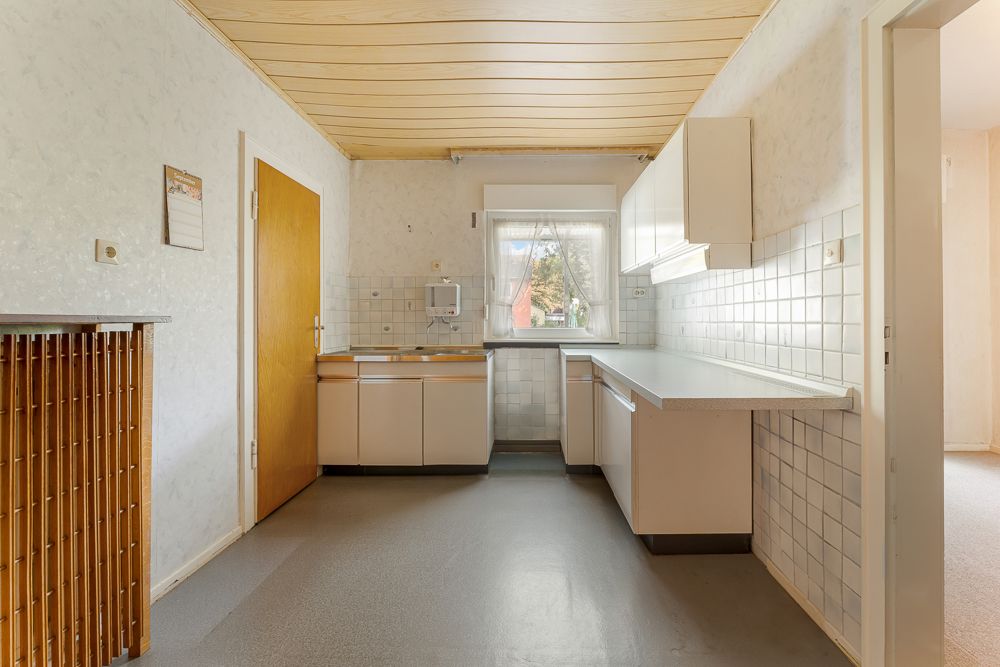 Helle Küche mit weißen Schränken, Holzdecke und Fenster, durch das Tageslicht einfällt.