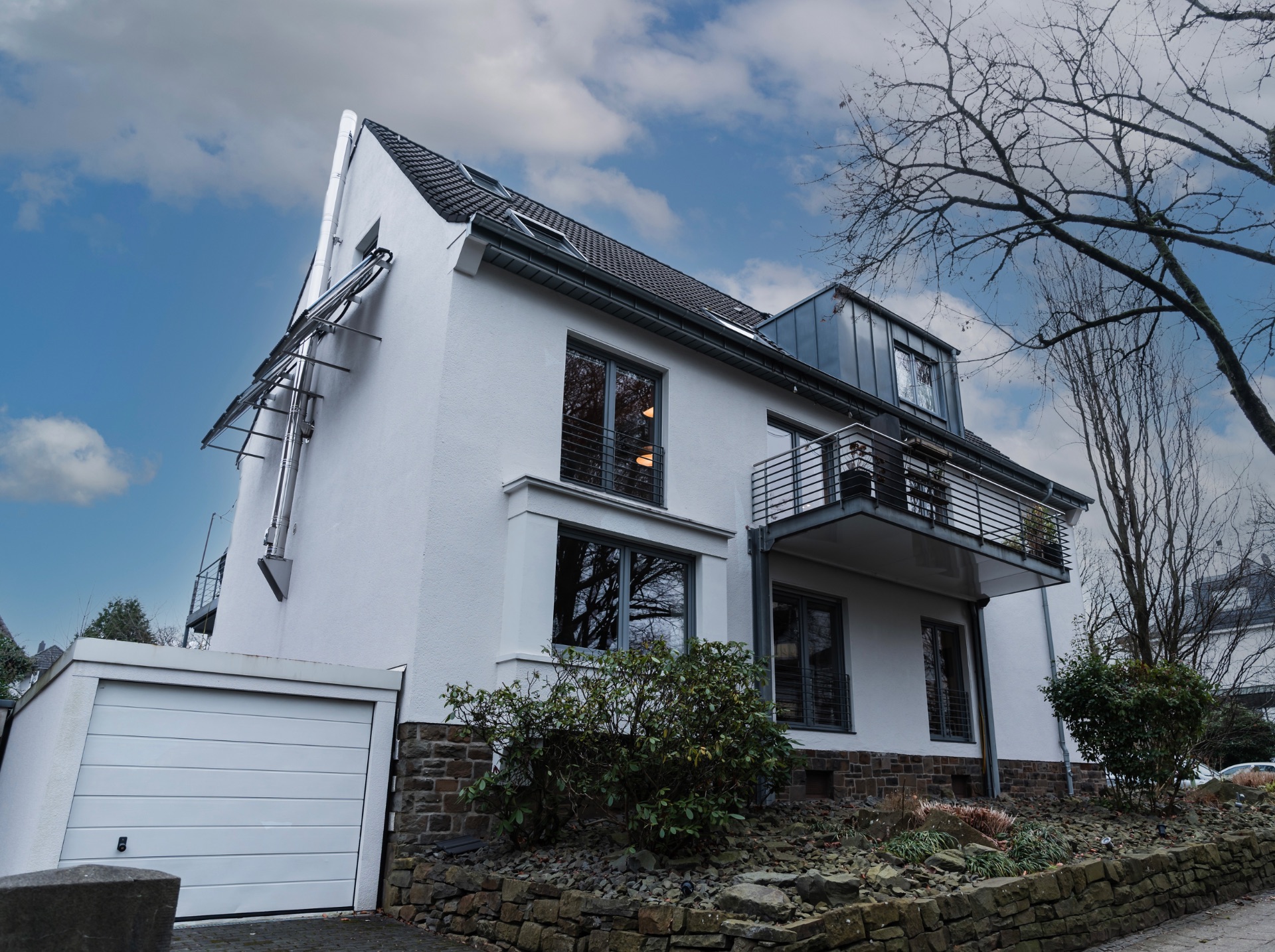 Modernes weißes Wohnhaus mit Garage, Balkon und Steingarten an der Vorderseite.
