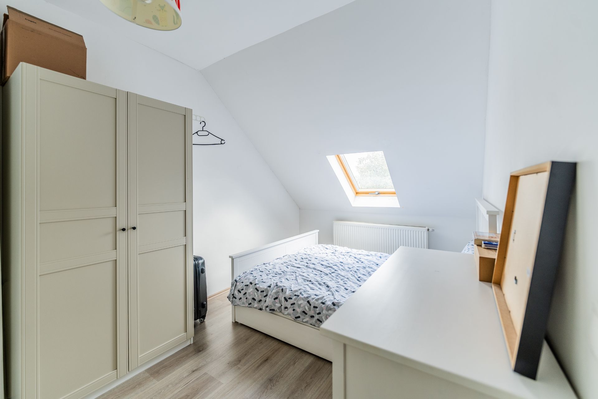 Helles Schlafzimmer mit Doppelbett, Kleiderschrank und Dachfenster.