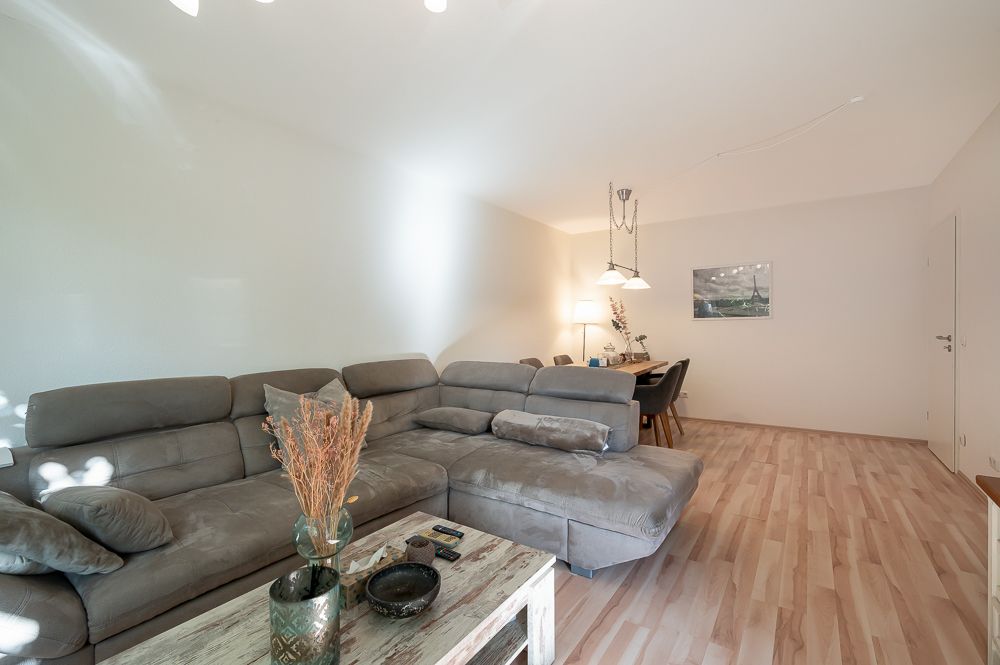 Helles Wohnzimmer mit grauem Sofa, Holztisch und Essbereich mit Tisch und Stühlen.
