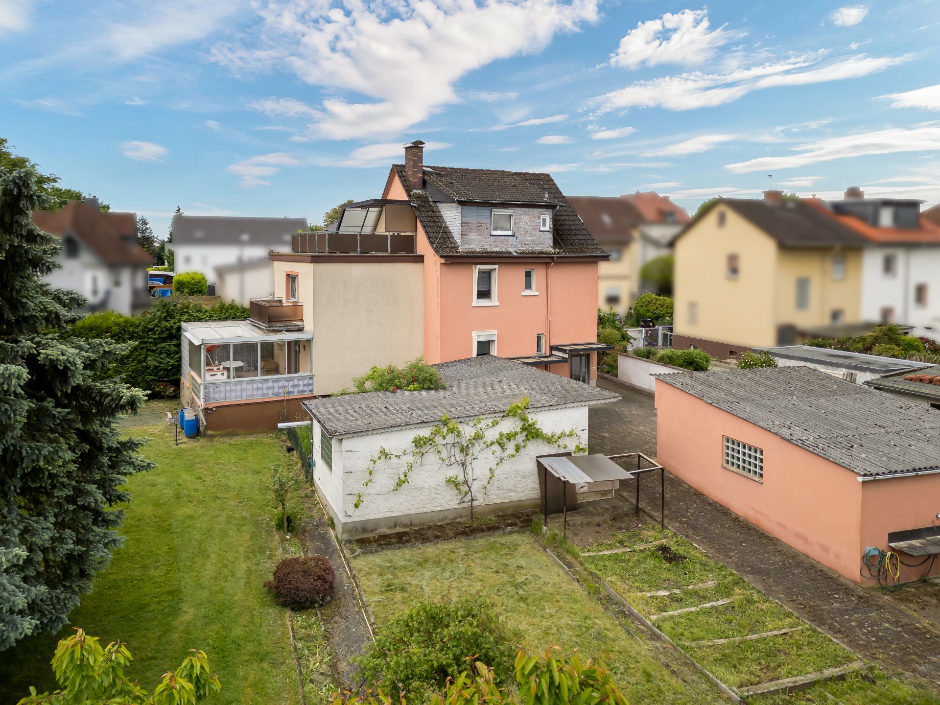 Ein rosa Wohnhaus mit Nebengebäuden und Garten, umgeben von weiteren Häusern.