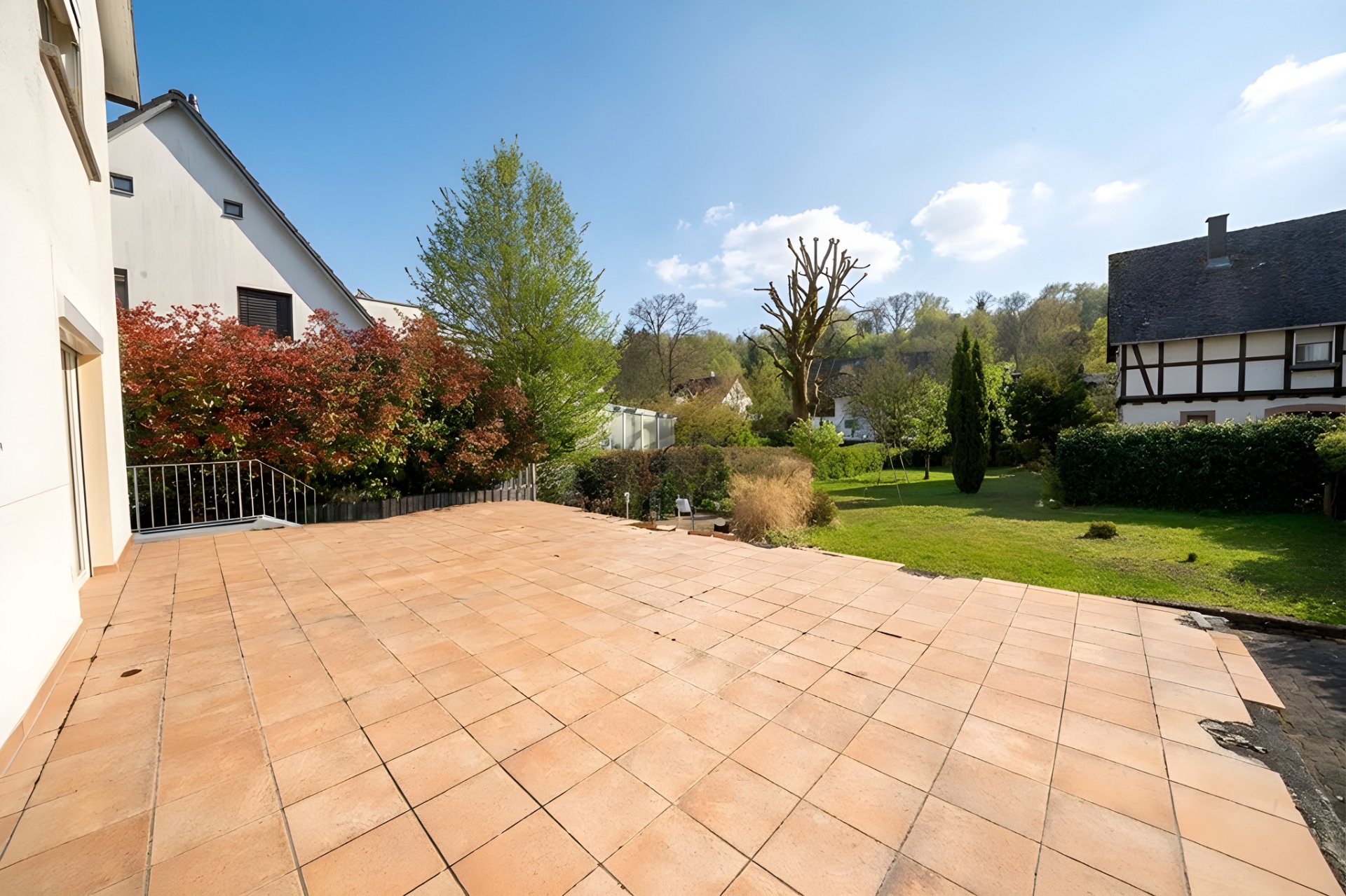Große geflieste Terrasse mit Blick auf Garten und Nachbarhäuser.