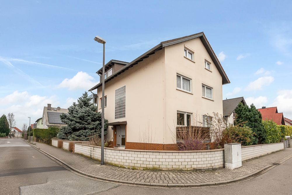 Eckhaus mit beigem Putz, Satteldach und Vorgarten an einer ruhigen Wohnstraße.