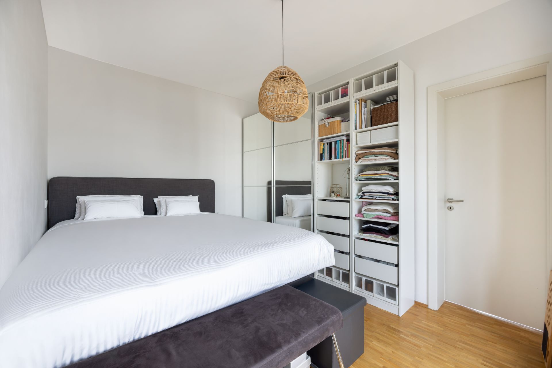 Helles Schlafzimmer mit Doppelbett, Kleiderschrank mit Spiegel und offenem Regal.