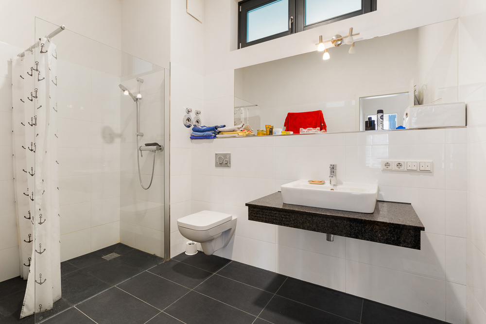 Modernes Badezimmer mit begehbarer Dusche, Wand-WC und Waschbecken vor großem Spiegel.