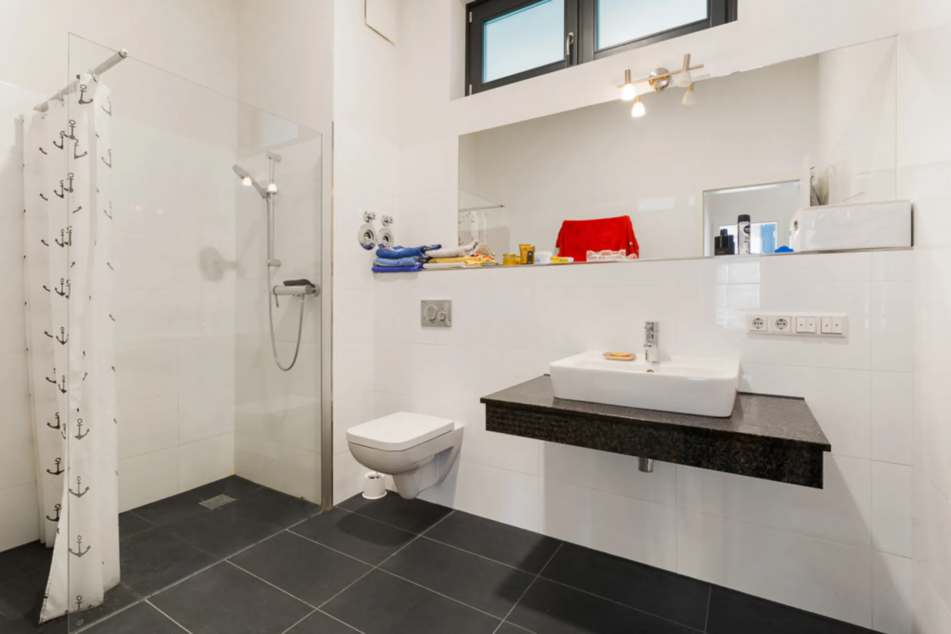 Modernes Badezimmer mit begehbarer Dusche, Wand-WC und Waschbecken vor großem Spiegel.