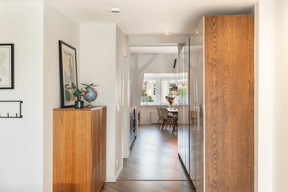 Heller Flur mit Holzschrank, Wandbild und Blick in ein Esszimmer mit großem Fenster.