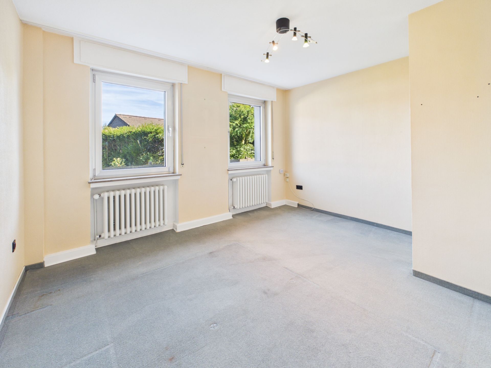 Leeres Zimmer mit zwei Fenstern, Heizkörpern und hellen Wänden.