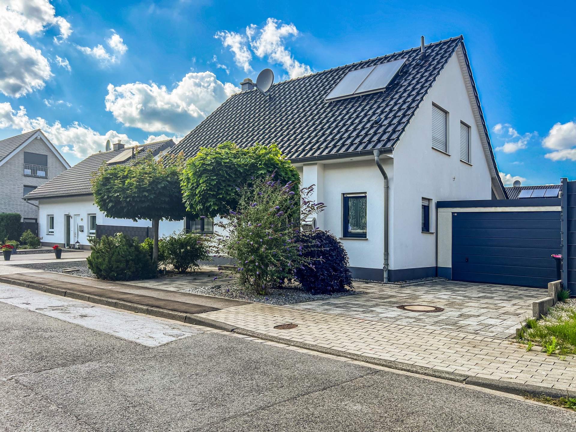 Modernes Einfamilienhaus mit dunklem Dach, Garage und gepflegtem Vorgarten an einer ruhigen Straße.
