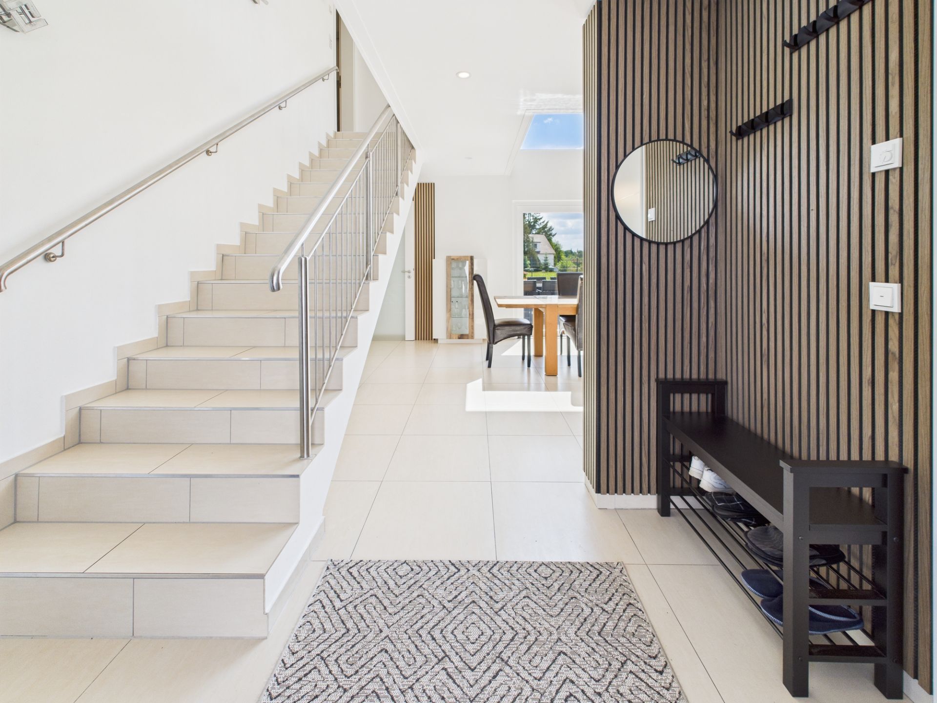 Heller Flur mit Treppe, Sitzbank, rundem Spiegel und Blick in das Esszimmer.