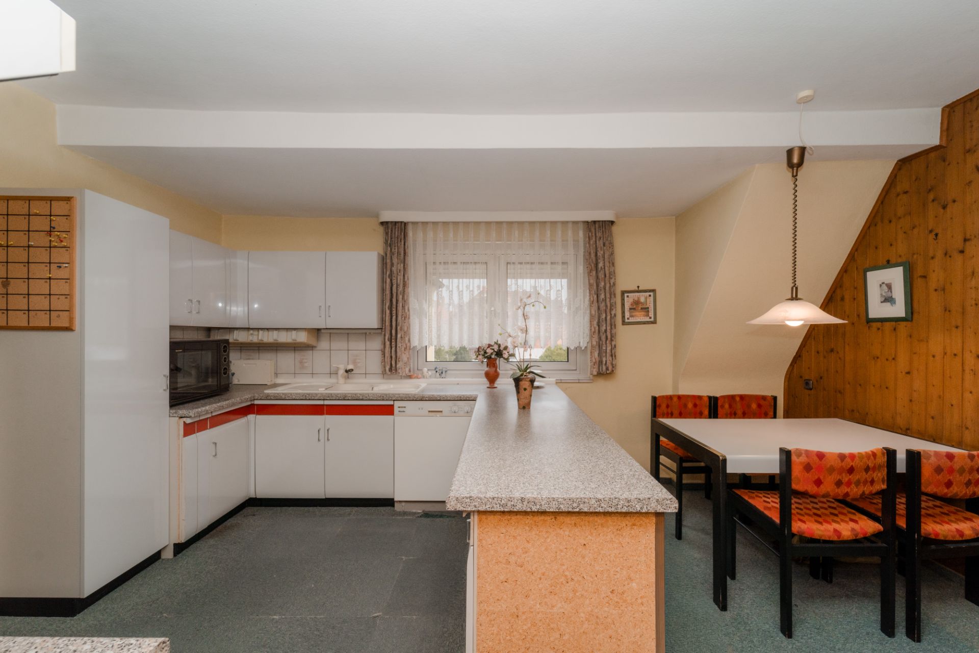 Küche mit Eckbank, Esstisch, Hängelampe und großem Fenster mit Gardinen.