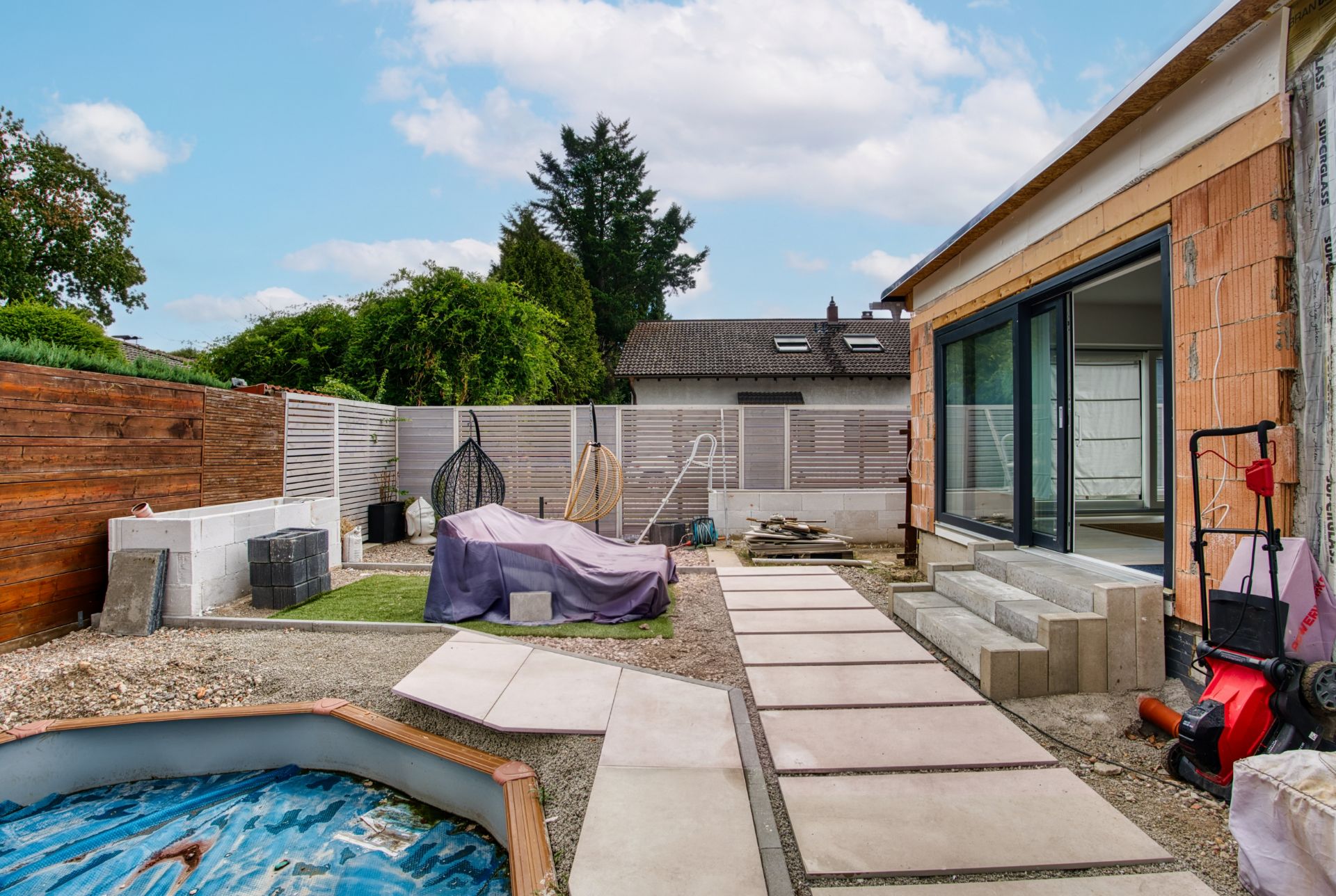 Gartenbereich mit Terrasse, Liegestühlen, Bauarbeiten und offenem Swimmingpool sichtbar.