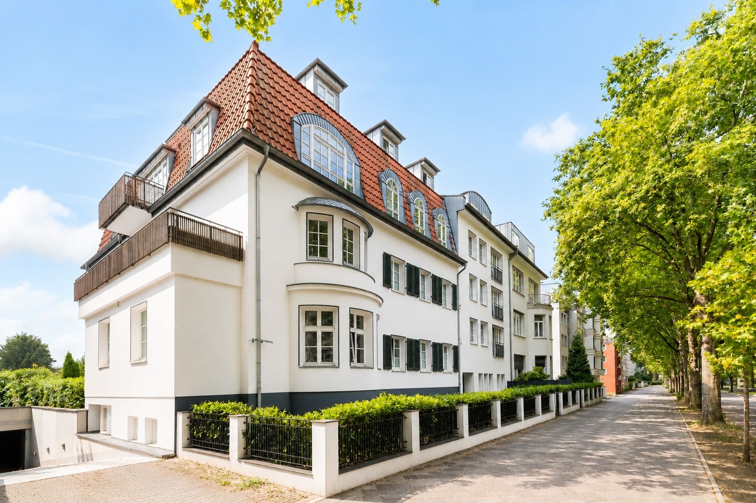 Wohnhaus mit rotem Dach, weißen Wänden und mehreren Fenstern an einer Baumallee.