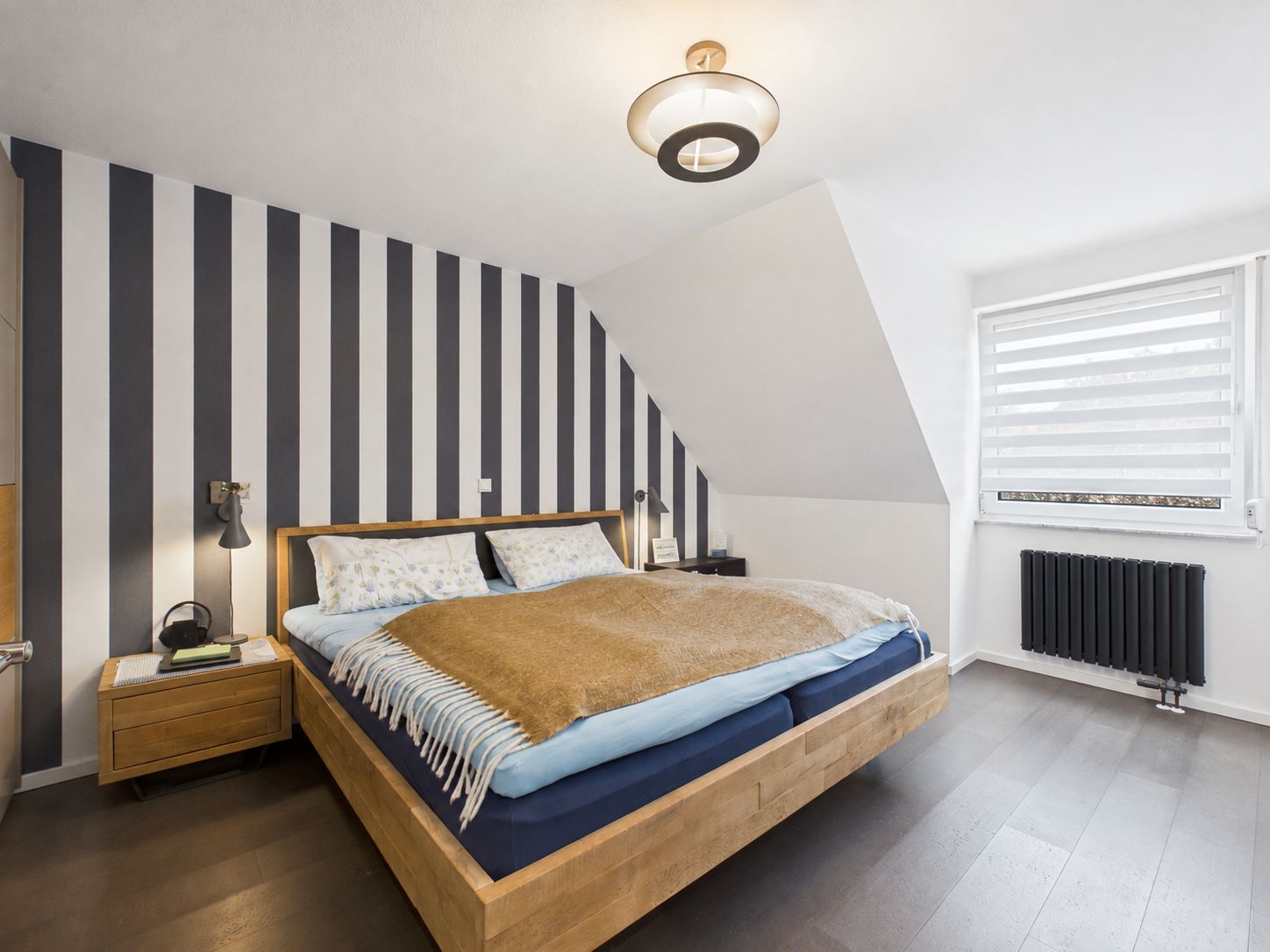 Modernes Schlafzimmer mit gestreifter Wand, Holzbett und großem Fenster mit Jalousie.