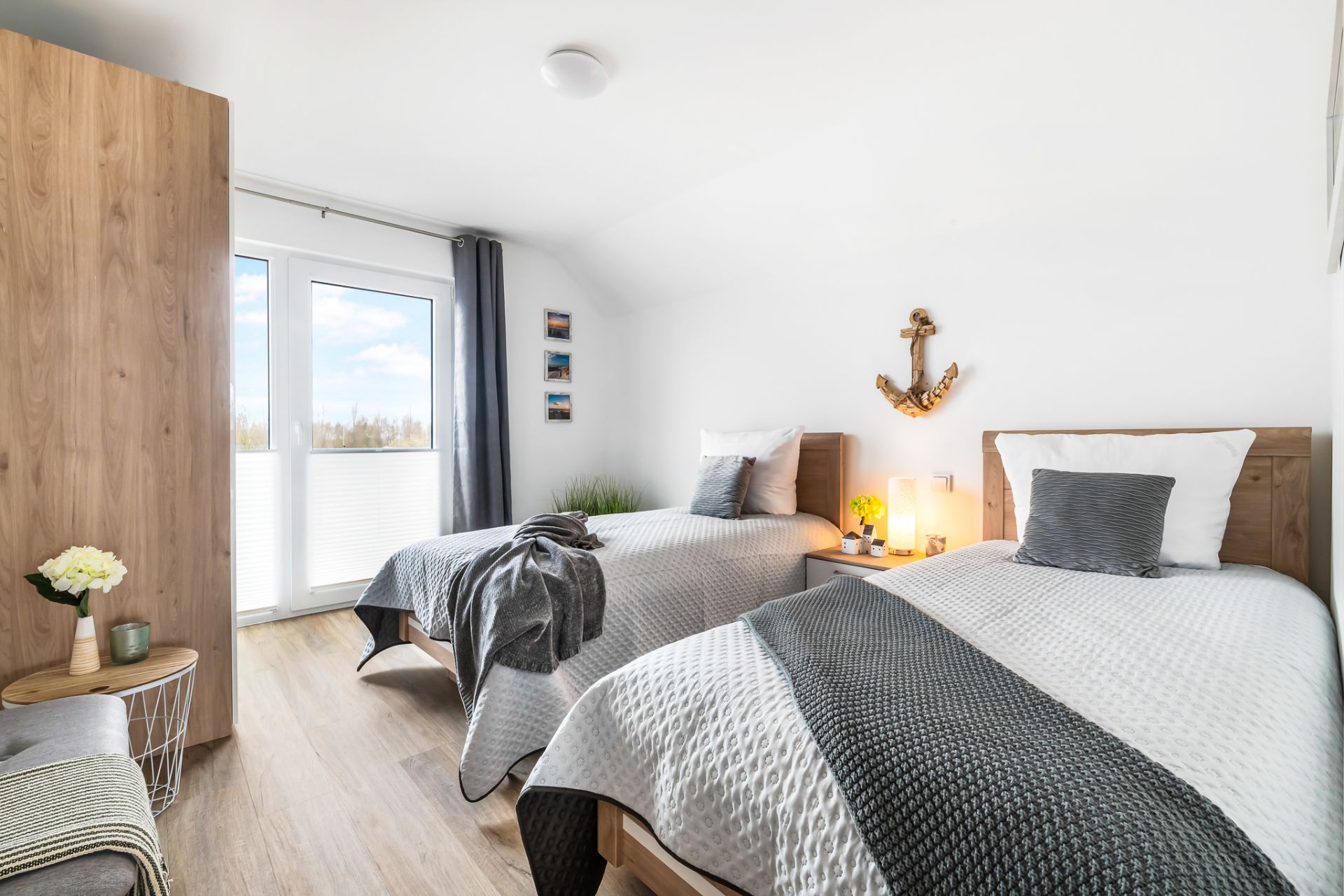 Helles Schlafzimmer mit zwei Einzelbetten, Nachttisch, Fenster und Dekor an der Wand.