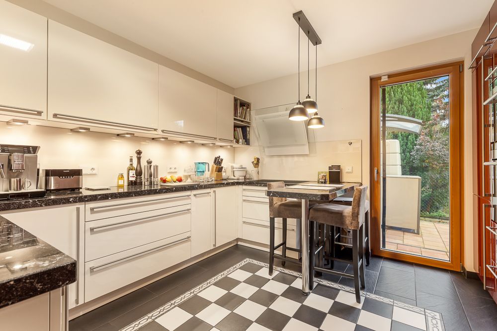 Moderne weiße Küche mit Esstisch, Hängelampen und Zugang zur Terrasse.