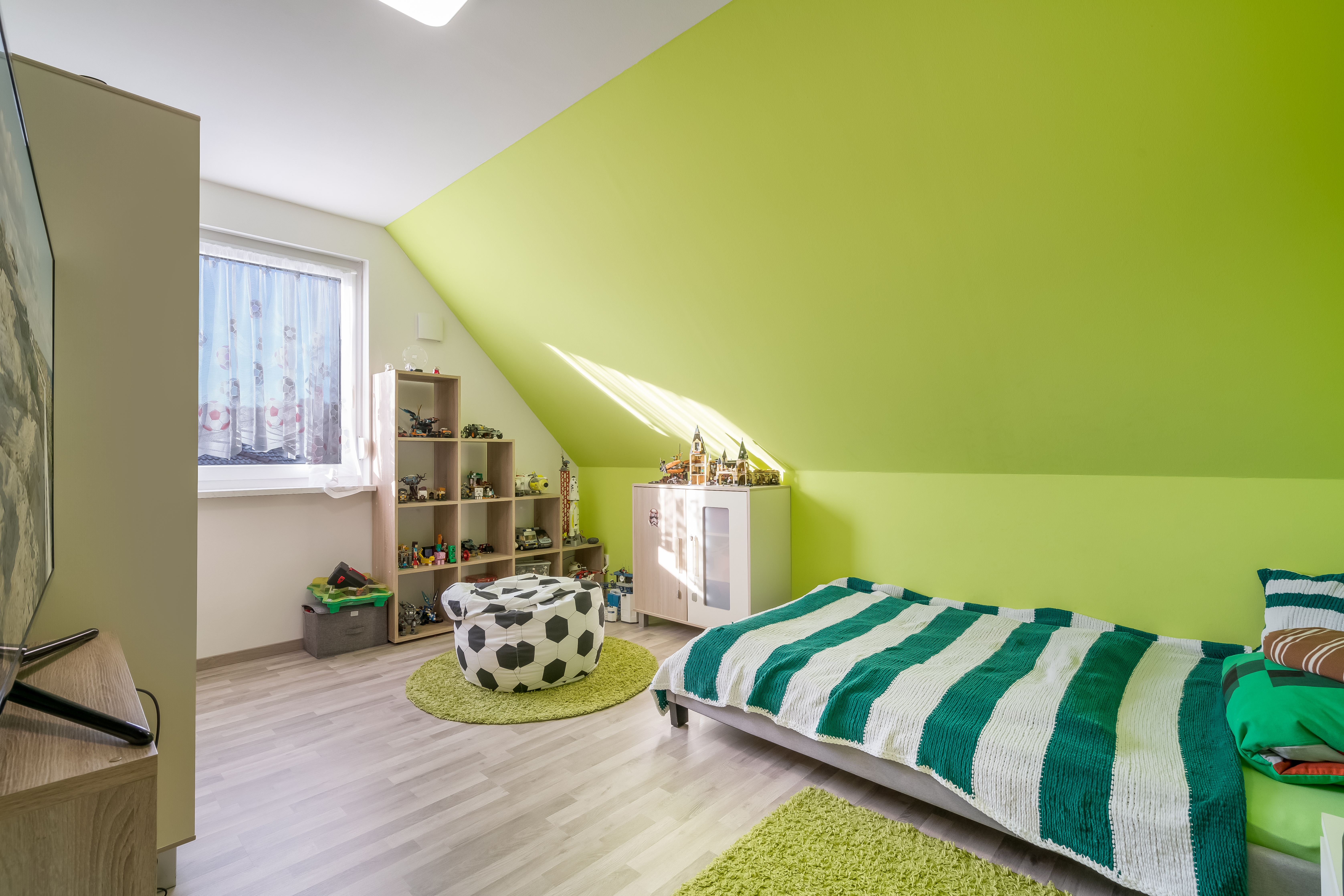 Helles Kinderzimmer mit grün gestrichener Wand, Bett, Regal und Spielzeug.