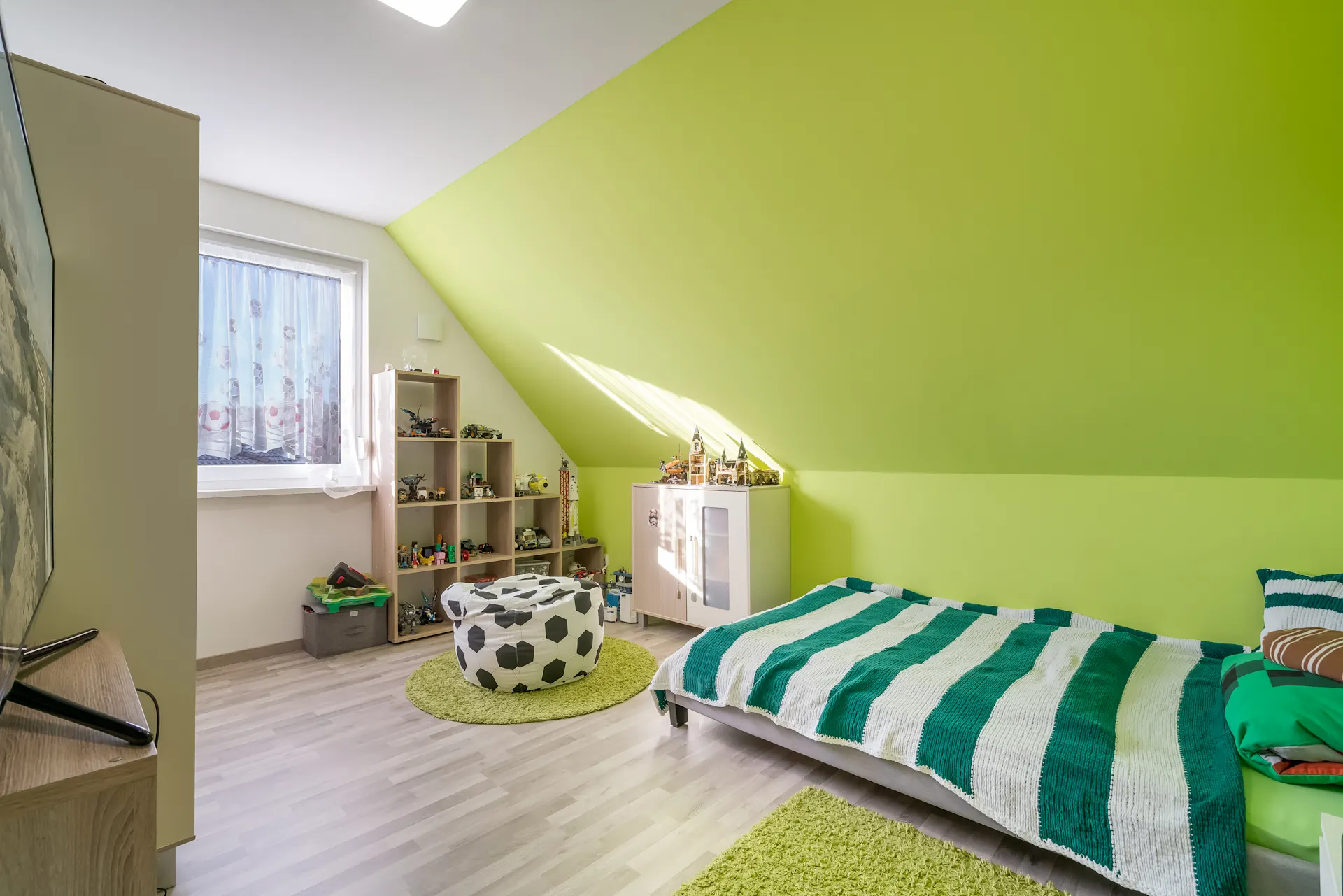 Helles Kinderzimmer mit grün gestrichener Wand, Bett, Regal und Spielzeug.