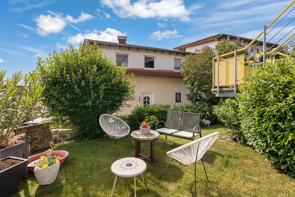 Garten mit Rasen, Gartenmöbeln und Blick auf ein Wohnhaus bei sonnigem Wetter.