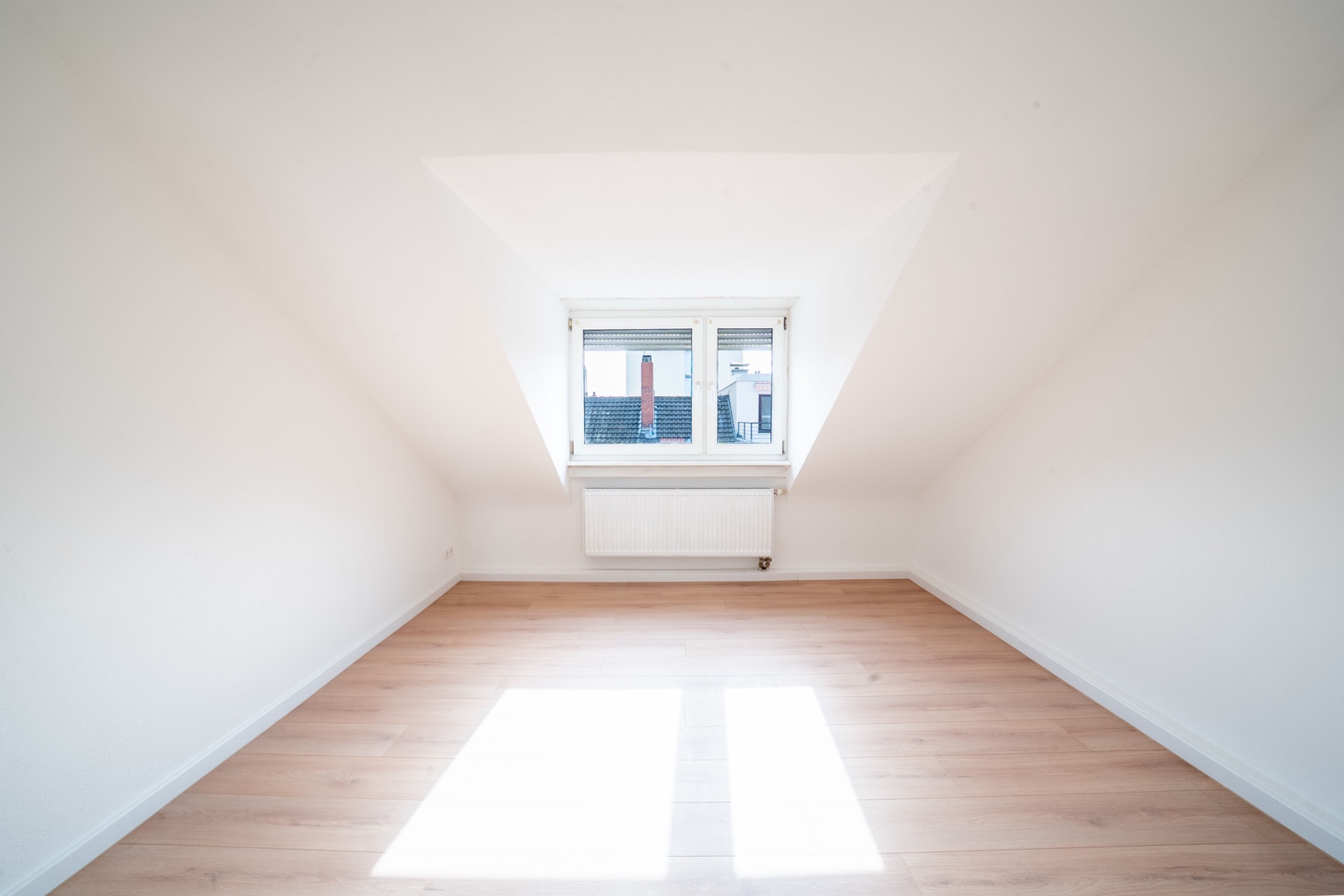 Helles, leeres Zimmer mit Dachfenster, weißer Wand und hellem Holzboden.