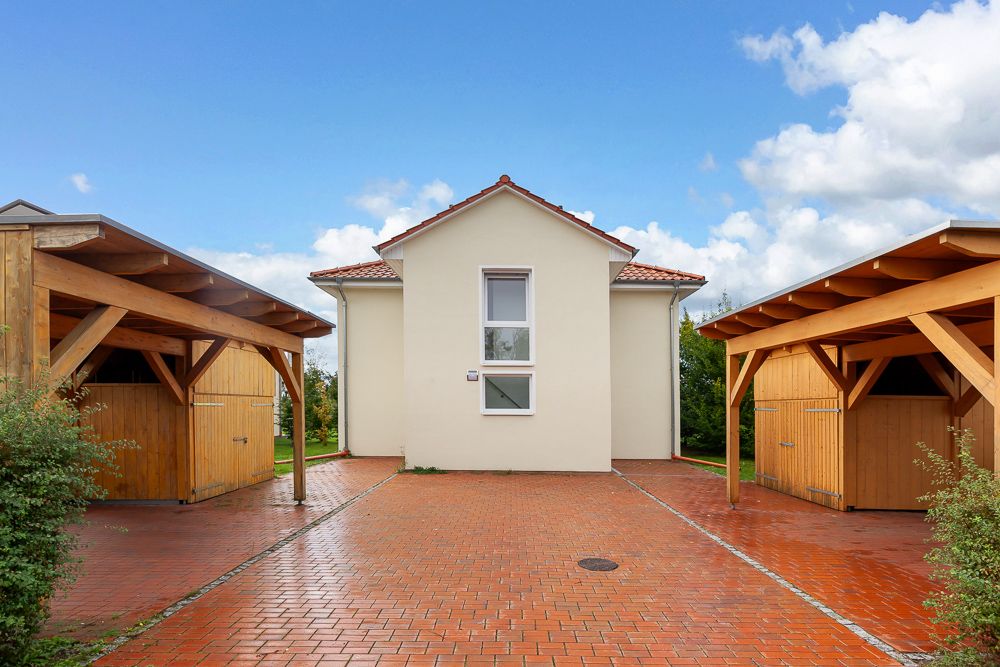 Helles Wohnhaus mit zwei Carports und rotem Pflasterweg davor.