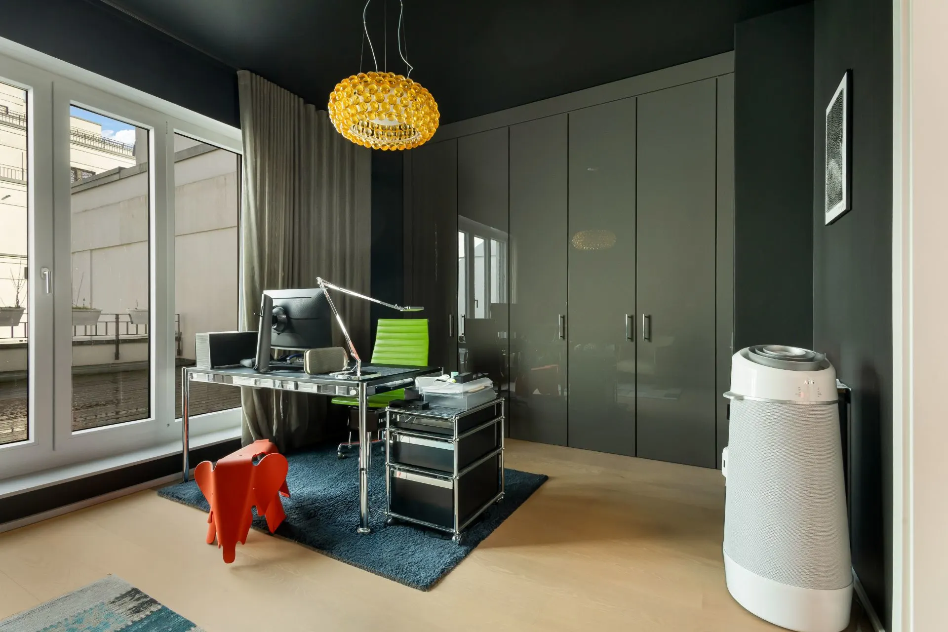 Modernes Arbeitszimmer mit großem Schreibtisch, grünem Stuhl und grauen Einbauschränken.