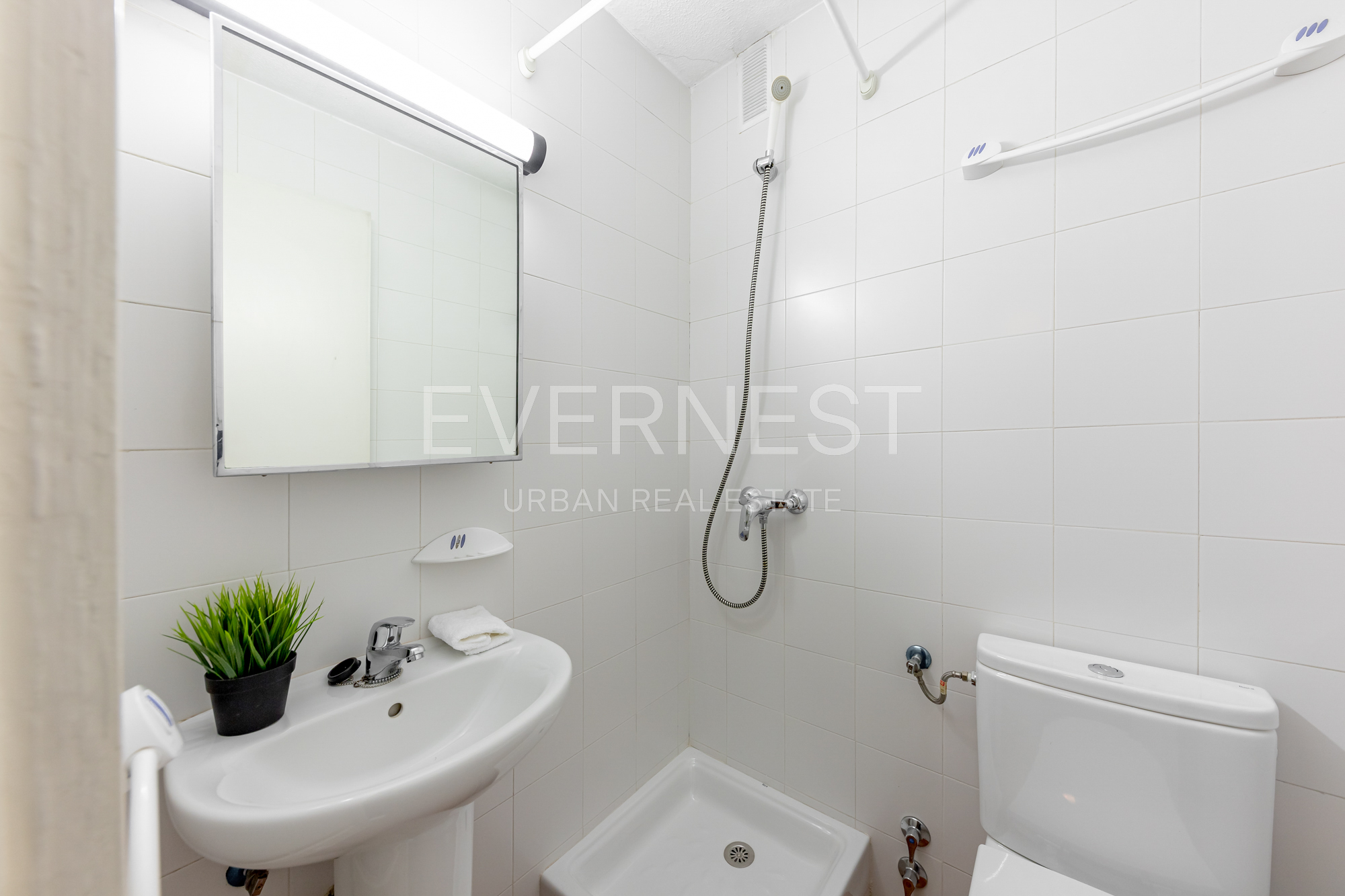 Kleines Badezimmer mit Waschbecken, Spiegel, Dusche und Toilette, weiße Fliesen.