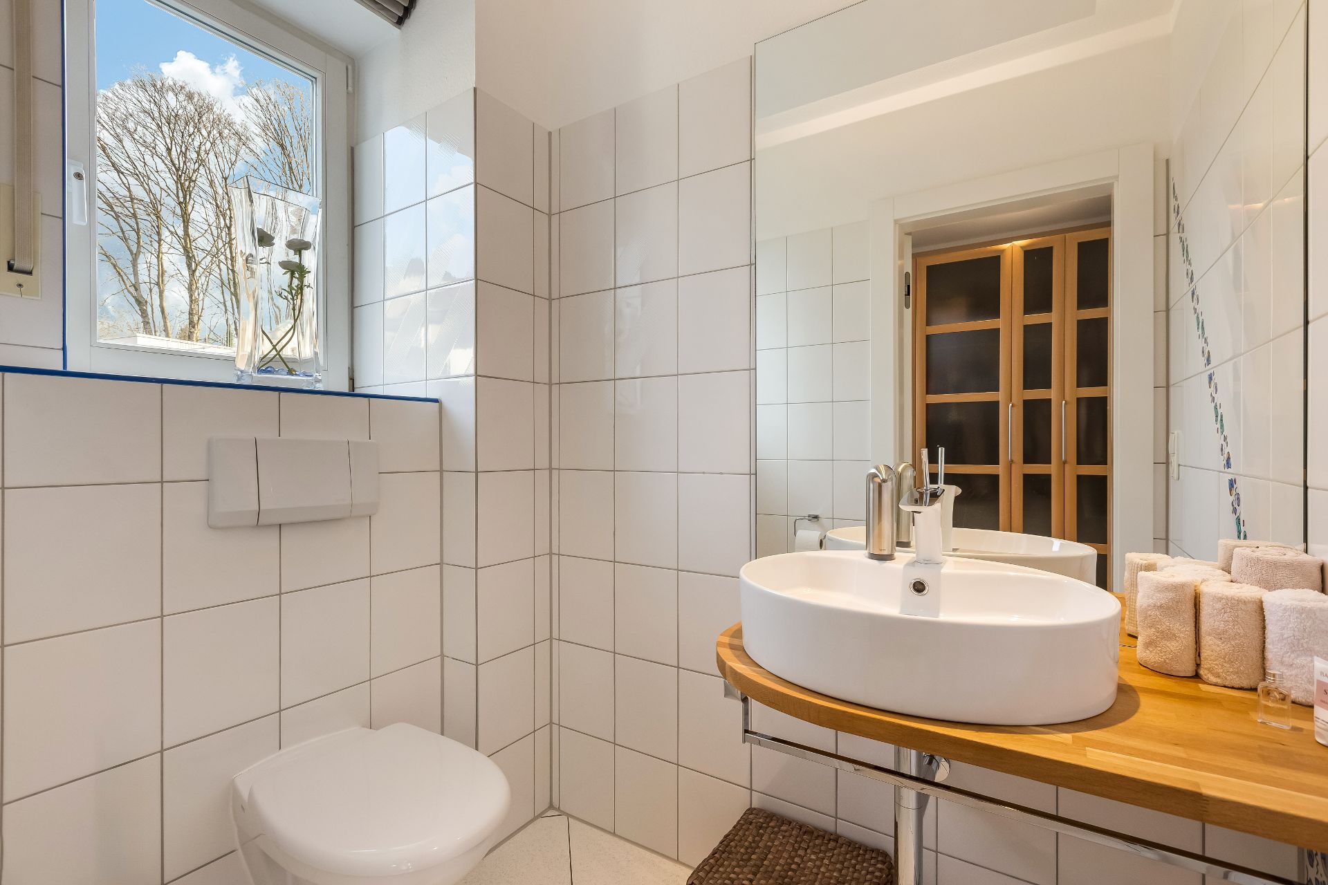 Modernes Badezimmer mit rundem Waschbecken, Holzablage, Spiegel und Fenster.