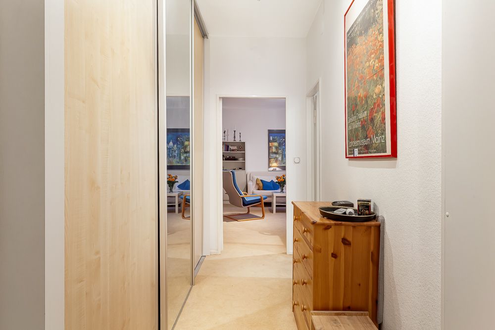 Heller Flur mit Holzkommode, Spiegel-Schrank und Blick in ein Wohnzimmer mit Sesseln.