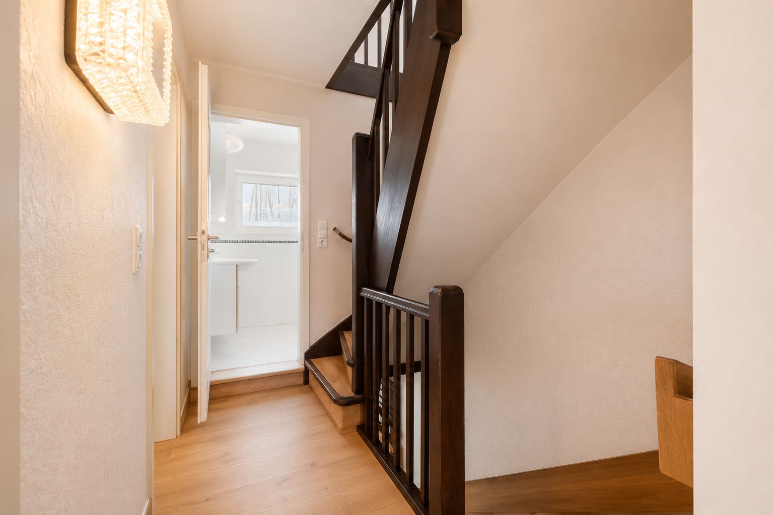Heller Flur mit Holztreppe und offenem Zugang zu einem angrenzenden Raum mit Fenster.
