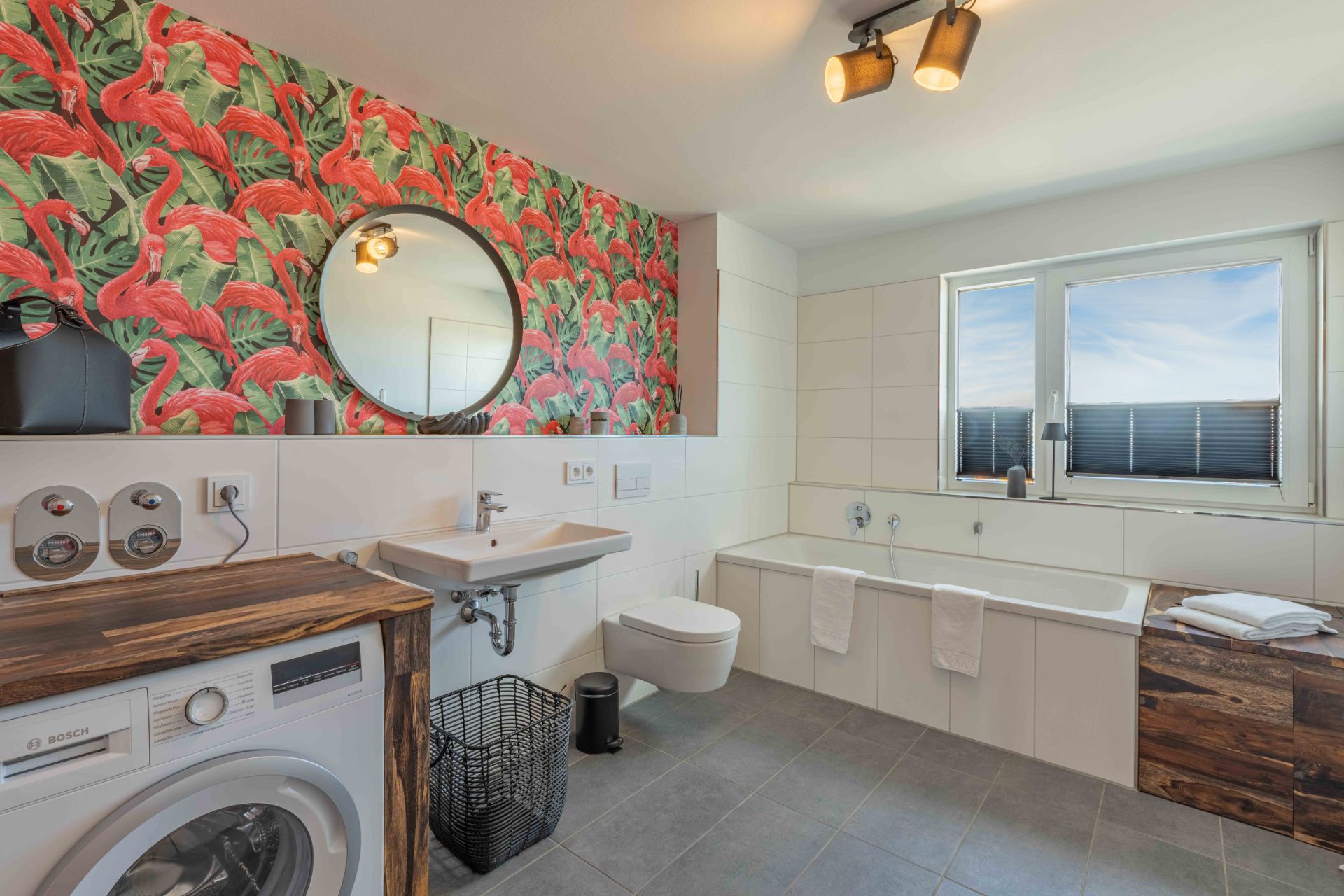 Modernes Badezimmer mit Flamingo-Tapete, Badewanne, Waschmaschine und großem Fenster.