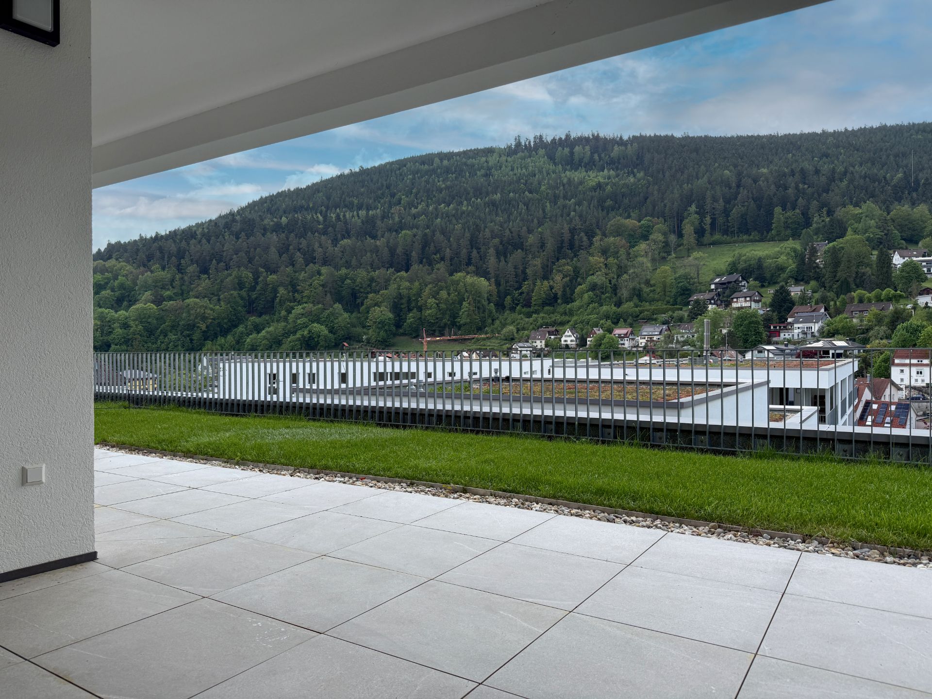 Überdachte Terrasse mit Blick auf Berge, Wald und Wohnhäuser.