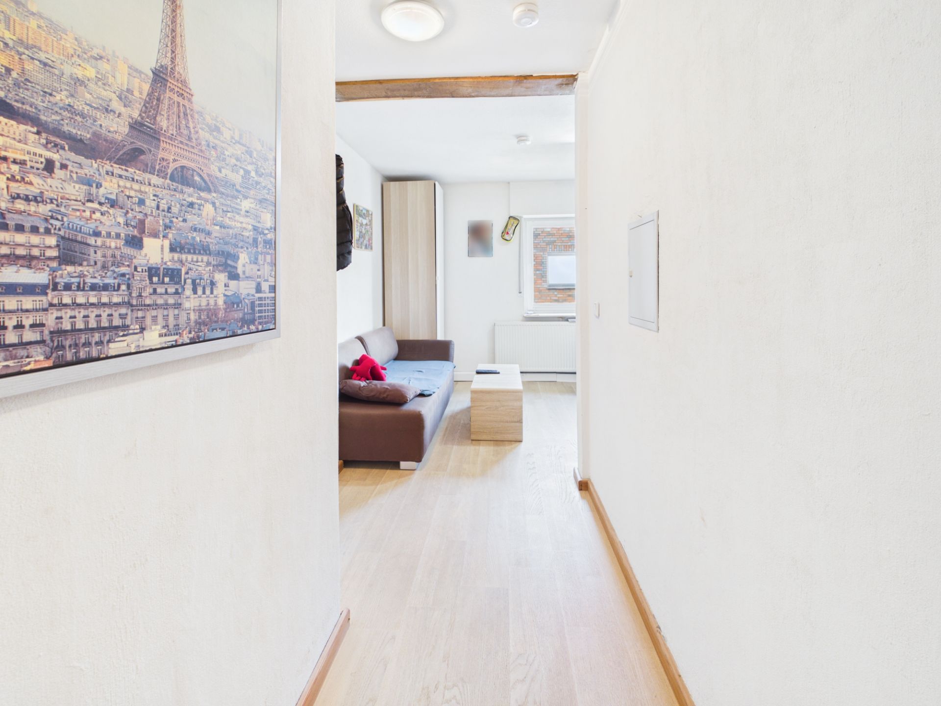 Heller Flur mit Holzboden, an der Wand ein großes Bild, hinten ein Wohnzimmer mit Sofa und Tisch.